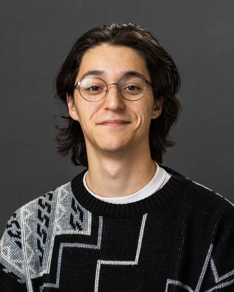 Person smiling with glasses in a gray sweater for a headshot.